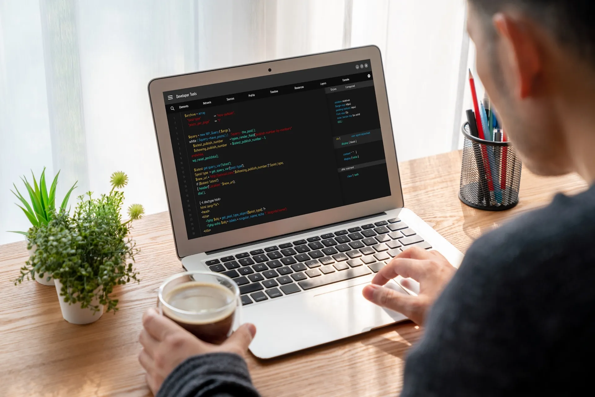 Programista z kawą w dłoni pisze kod na laptopie